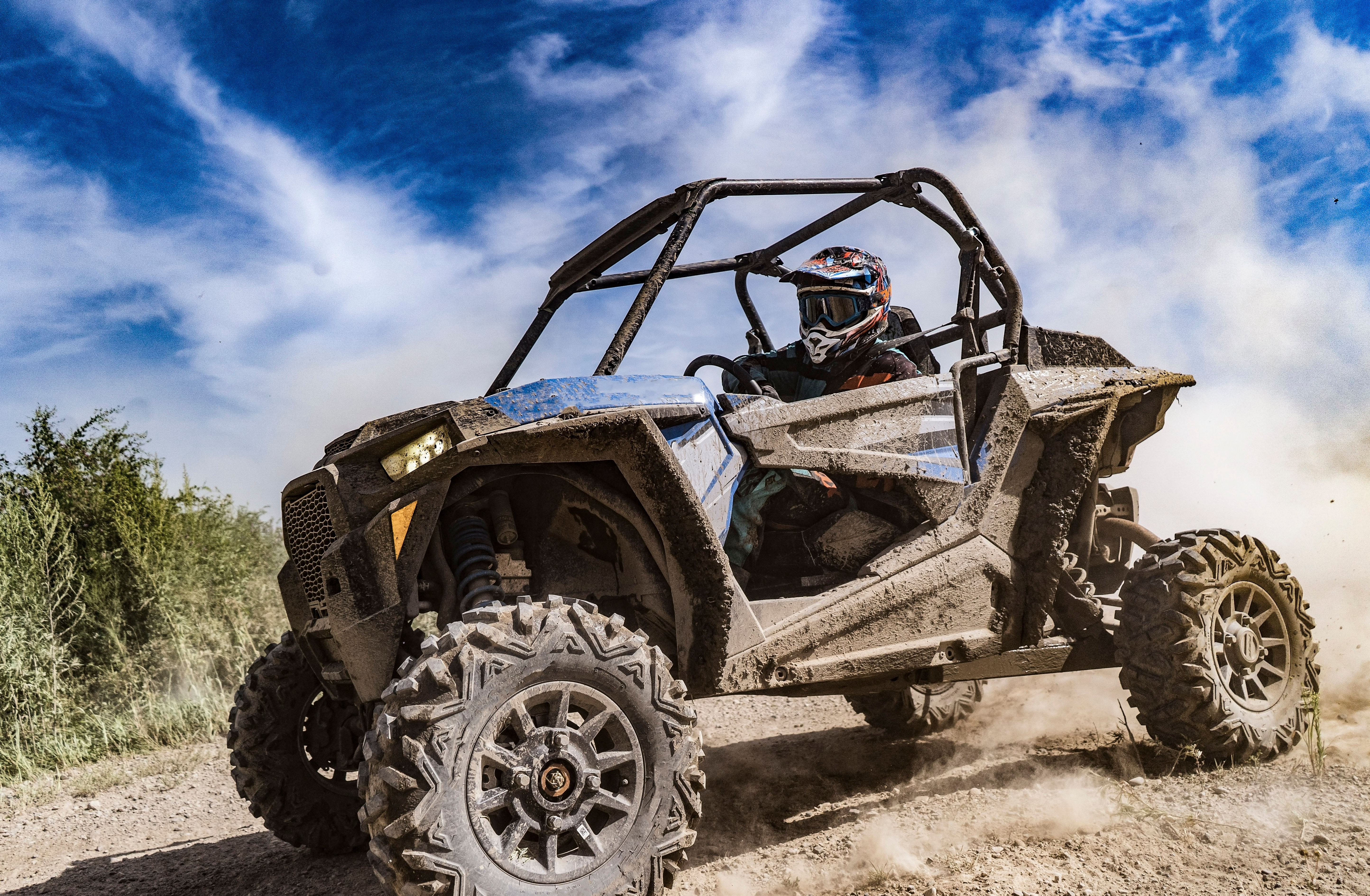 helmeted rider sitting in a dirt-covered UTV