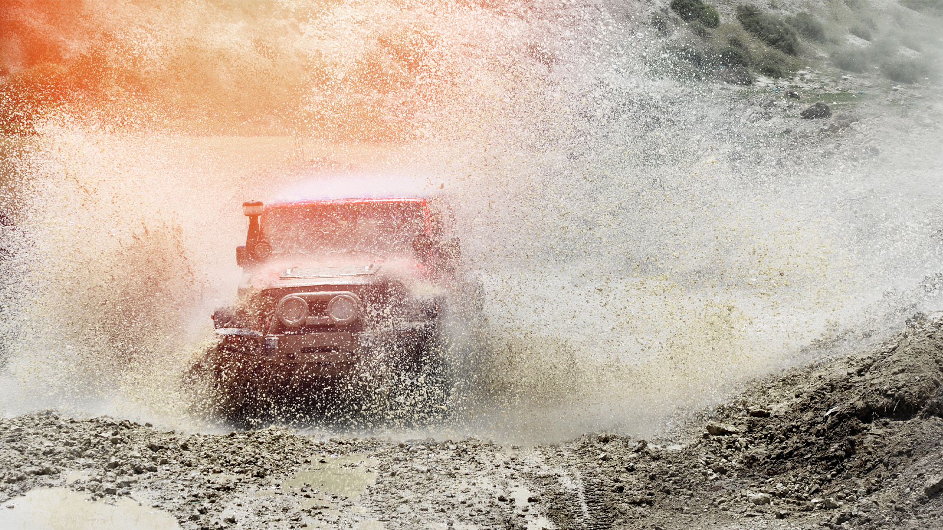 red vehicle spraying mud into the air